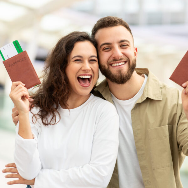 Man and Woman Holding Up Passports In Airport And Smiling At Camera
